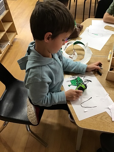 School Age 1 child sitting at the table with paper, markers, and a toy - the child is looking at a picture coloured while holding his toy