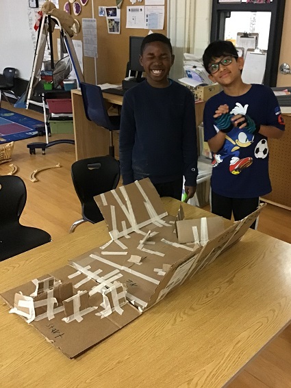 children standing in front of their marble run creation made out of cardboard and tape