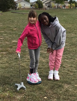 two childen standing giving a side hug to each other. One child standing using a cane as support