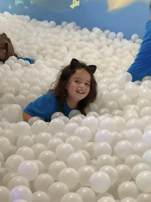 child covered in white balls inside of a ball pit.