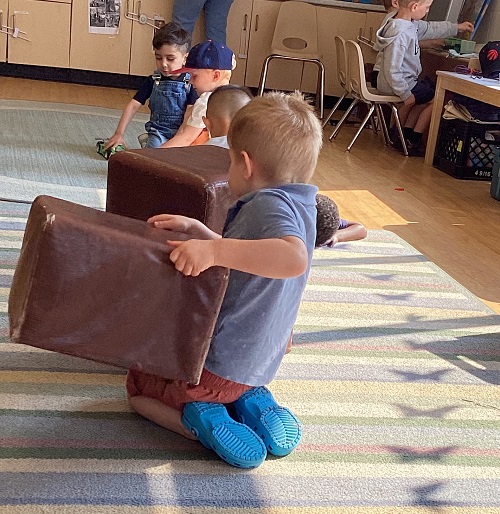 children on the floor moving brown ottomans around the classroom