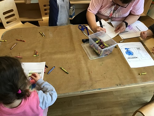 A child and an educator sitting at a table colouring