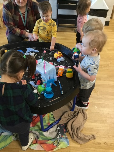 Children surrounding a tuff tray set up as a car wash