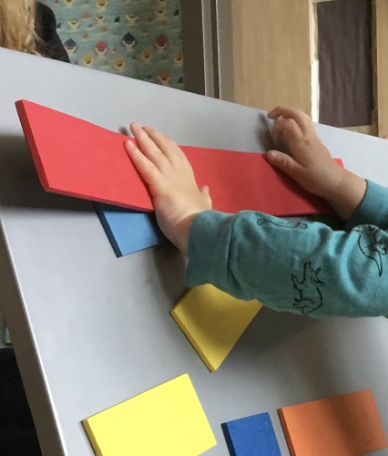 A child's hand pushing square colourful magnets on a tray