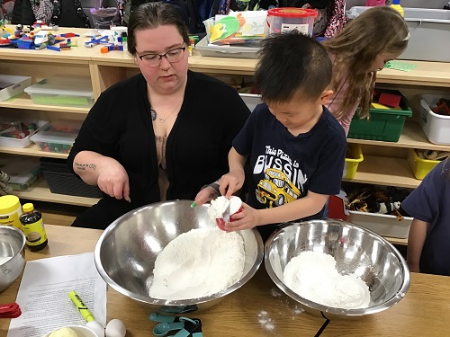 A child adding ingredients to a mixing bowl with an educator
