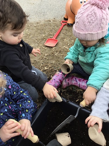Children sitting around a tuff tray full of soil, using shovels to scoop the soil 