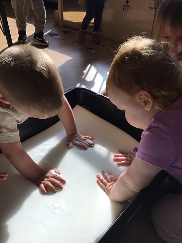 Children pushing hard on a foam piece in a sensory bin