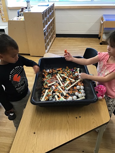 Two children playing in a sensory bin filled with Halloween themed items