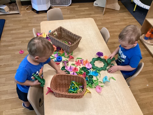 Two children at a table making a garden with plastic flowers, stems and petals