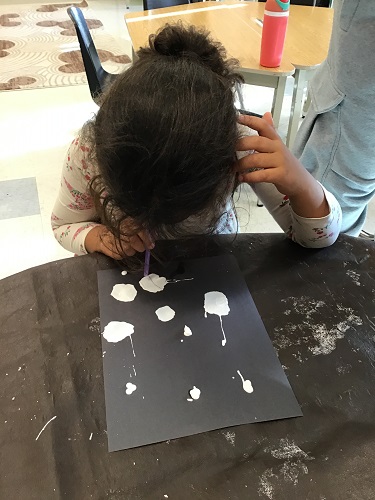 A child at a table using a straw to blow paint around on her paper