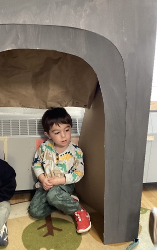A child sitting in a cave made out of a large box