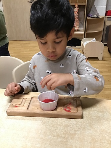 A child pinching sand from a paper cup and putting it on a letter plate