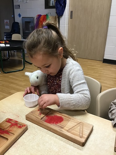 A child pinching sand from a paper cup and putting it on a letter plate
