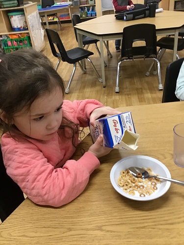 A child sitting at a table pouring milk into a bowl of cereal