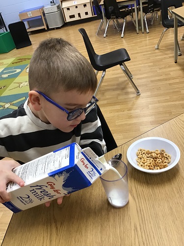 A child sitting at a table pouring milk into a cup
