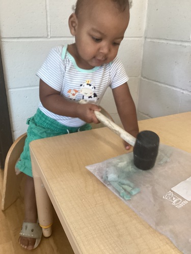 A child at a table using a mallet to crush chalk in a ziploc bag