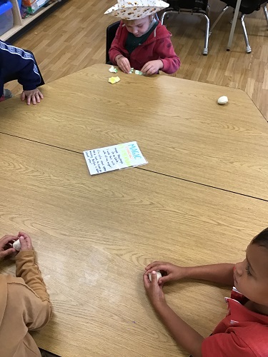 Children sitting at a table with a ball of playdough in their hands