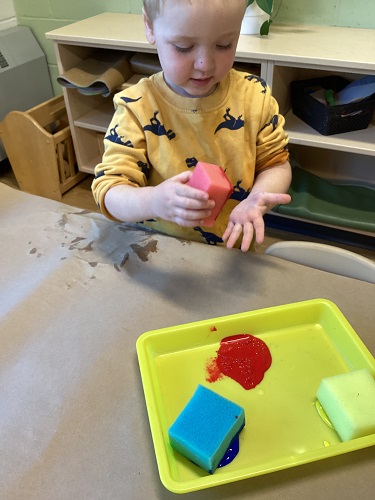A child sitting at a table using a sponge to paint his hands