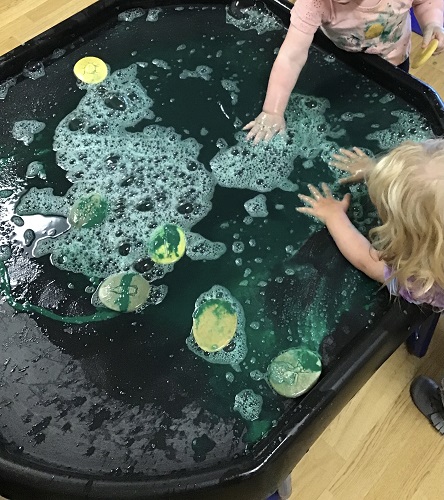 Children playing in the sensory table filled with soapy colourful water