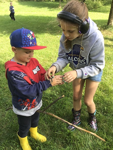 One School Age child holding the snake in another School Age 2 child's hand, another child standing in the background