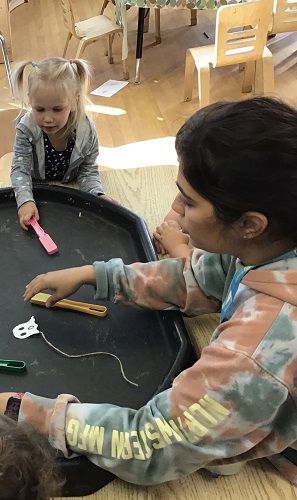 Preschool child sitting at the table beside an educator holding a magnetic wand, there is a ghost on the string in front of the educator