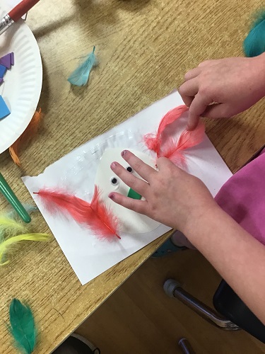 Child's hands gluing feathers to paper