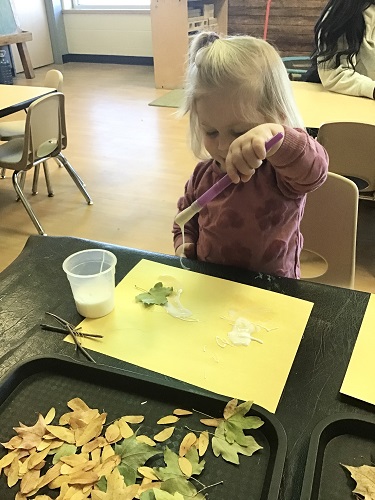 Child gluing leaves onto paper to make design 