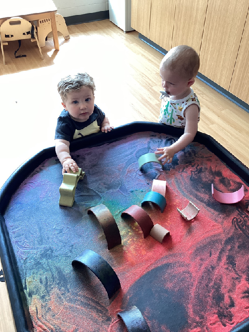Two children exploring a rainbow filled tuff tray.