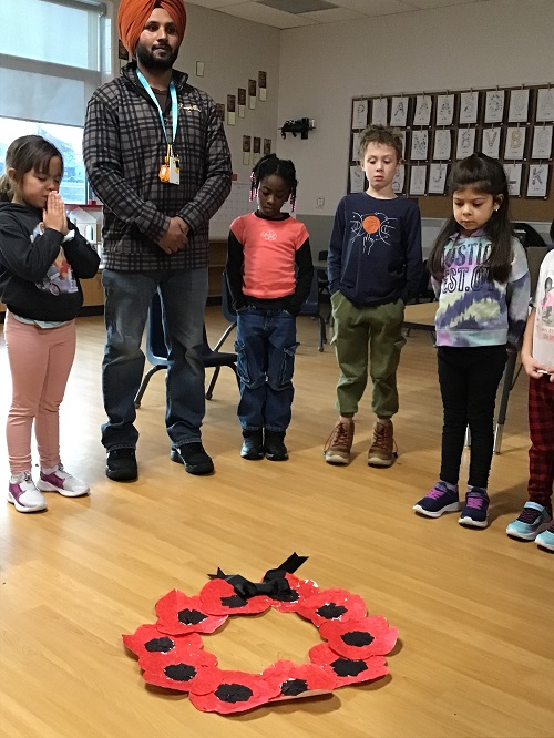 A group of school age children and an educator taking a moment of reflection around a poppy wreath