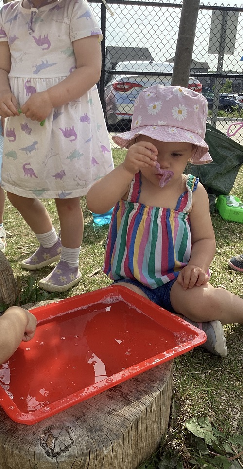 A child exploring a water tray on the playground.