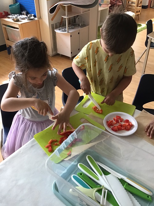2 School Age children cutting vegetables on a cutting board using child-safe knives