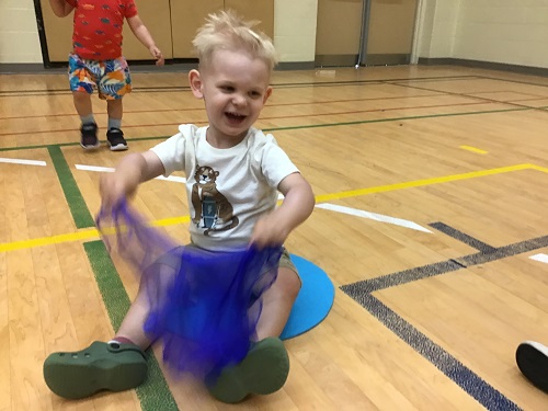A toddler playing with a coloured scarf