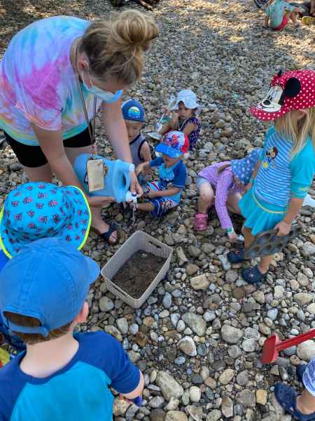 children watch educator pour water in bin full of mud