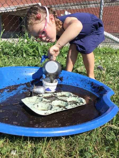 girl playing in a sled filled with mud outside