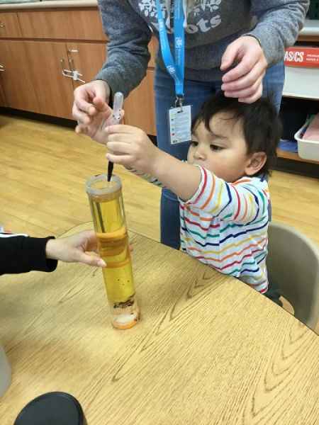 children adding coloured drops to a water filled tube