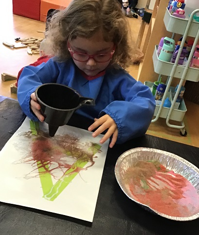 Child sprinkling sand on art