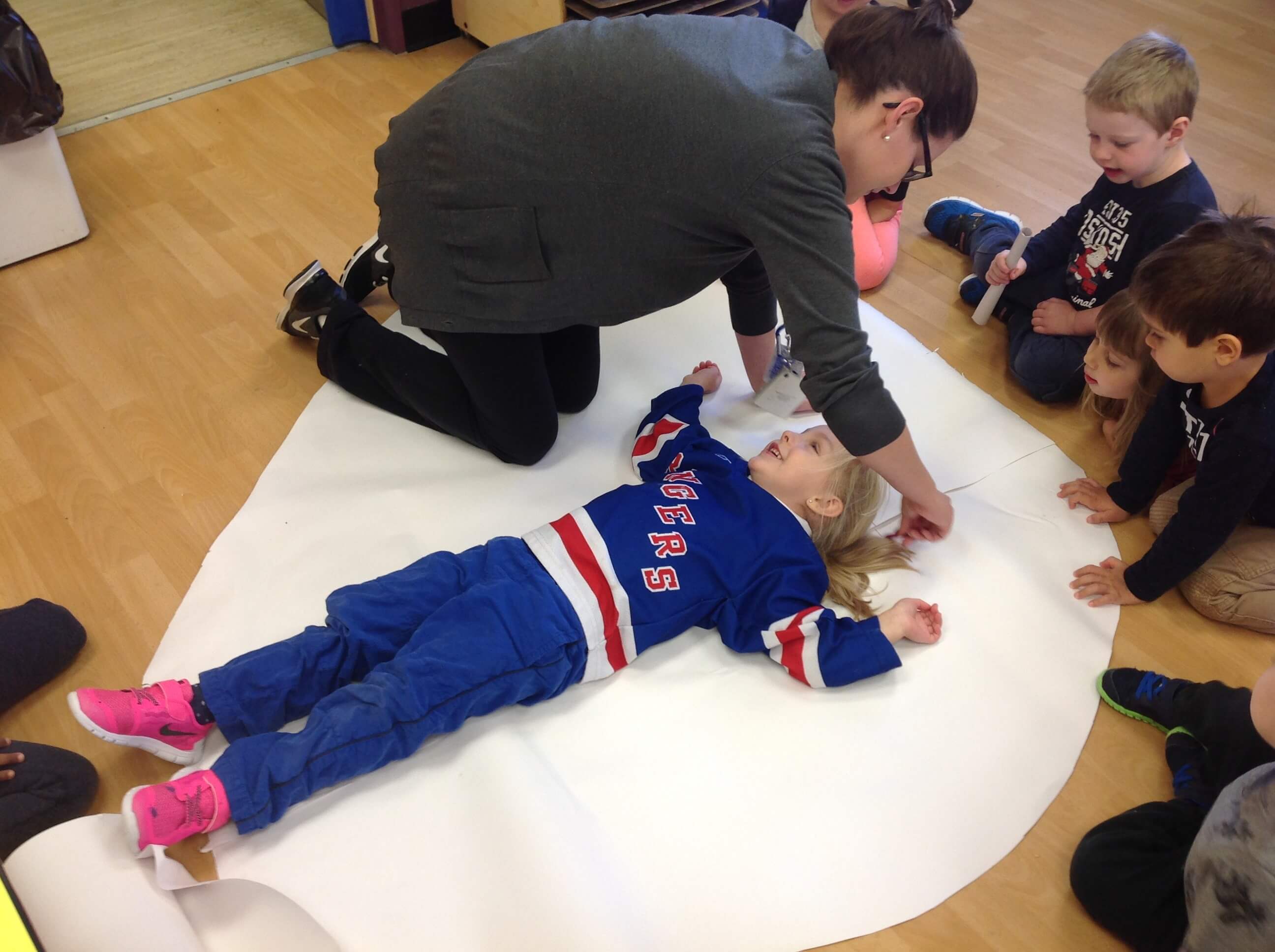educator tracing a preschooler on a large piece of paper