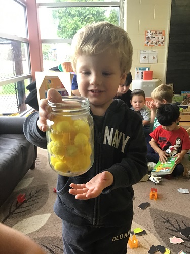 Preschool child holding up jar of yellow pom poms