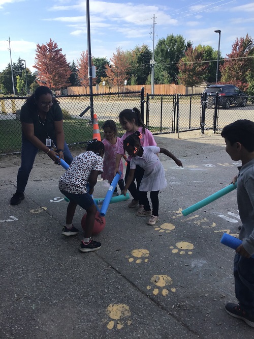 Children and educator playing a game of pool noodle hockey.