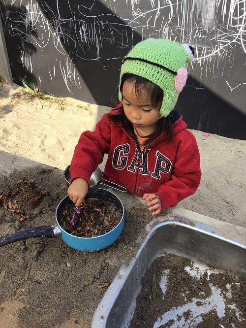 Child pretending to cook with outdoor sand. 