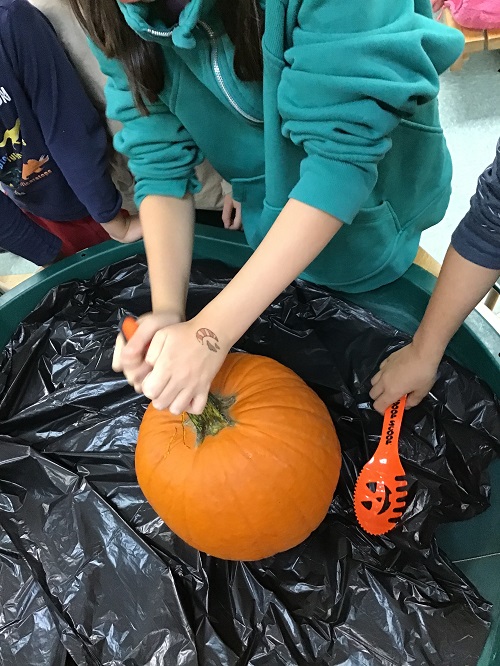 Child carving the top of a pumpkin.
