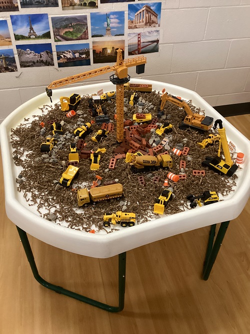 a tuff tray set up with crinkle paper, play bricks, play trucks and a play crane