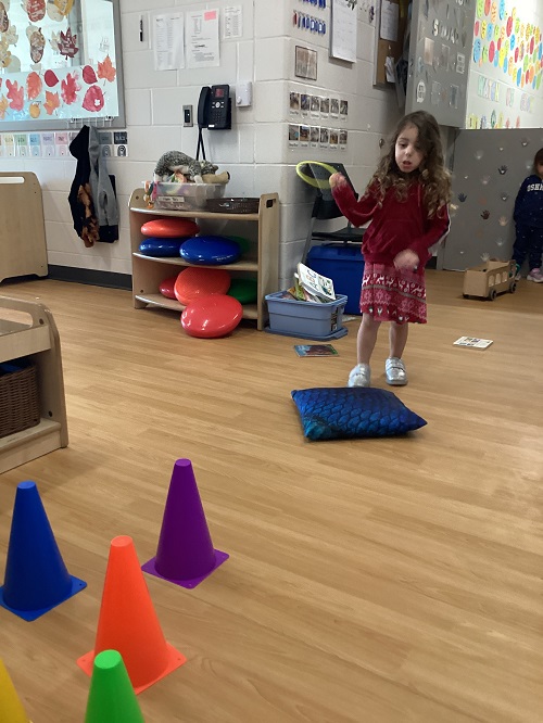 A preschool child participating in a ring toss game using pylons and rings