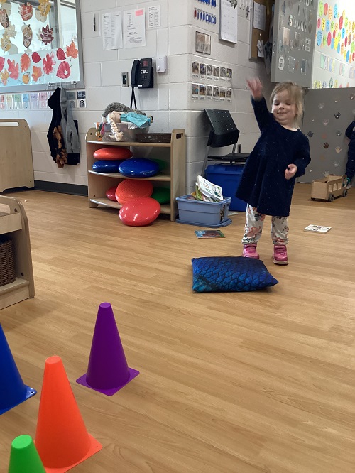 A preschool child participating in a ring toss game using pylons and rings