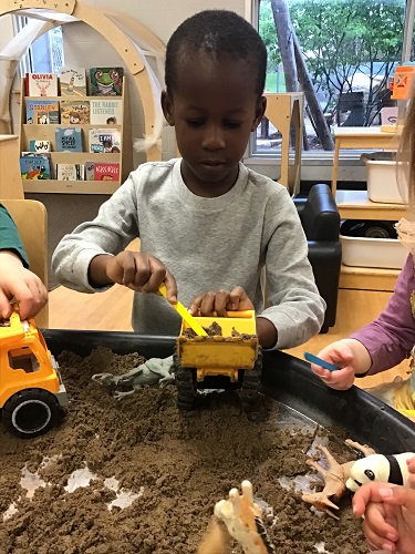Preschool child at the tuff tray with wet sand and trucks all around