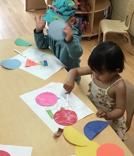 Two toddlers gluing paper shapes onto paper